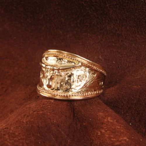 Gold ring with detailed engraved design on a brown background.