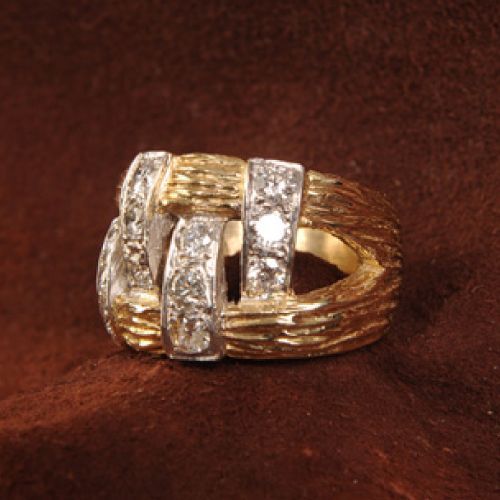 Gold ring with textured finish and diamond-studded white gold bands, on brown surface.