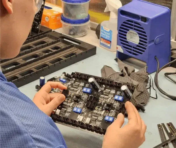 A man is sitting at a table working on a circuit board.