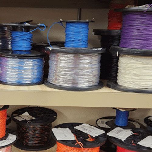 A shelf filled with spools of wire of different colors