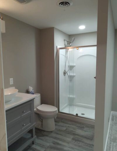 Bathroom with shower, vanity, and toilet. Light gray walls and flooring, white shower with clear glass door.