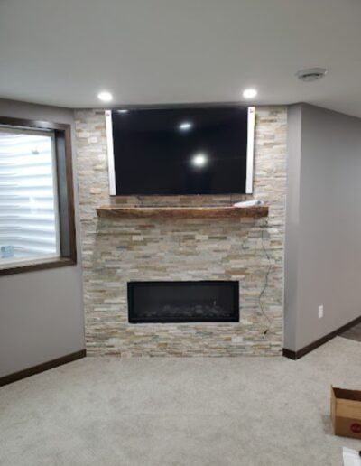 TV and electric fireplace set into a stone wall, with a wooden mantel.
