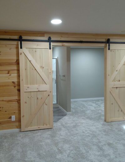 Barn doors, light wood with black hardware, open to a room with carpet and a doorway to another room.