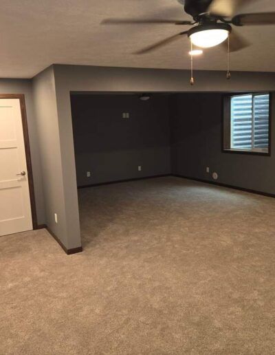 Empty room with gray walls and beige carpet. Dark gray alcove with a window. Ceiling fan.