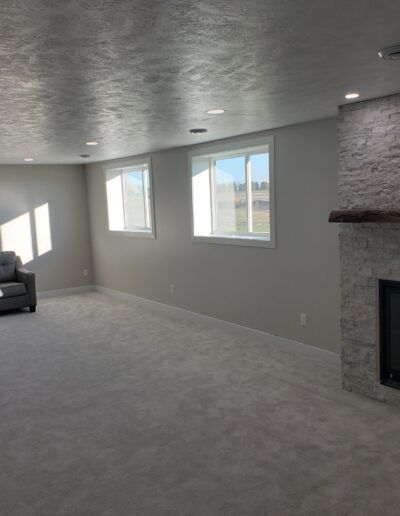 Empty finished basement with windows and fireplace. Light gray walls, carpet, and stone fireplace.