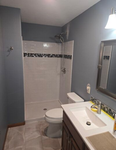 Bathroom with gray walls, white shower, toilet, dark wood vanity, and a mirror.