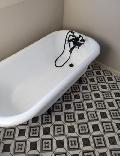 White claw-foot bathtub with black fixtures in a corner; black and gray patterned tile floor.