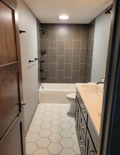 Bathroom with gray tile shower, white tub, black fixtures, and hexagon tile floor.