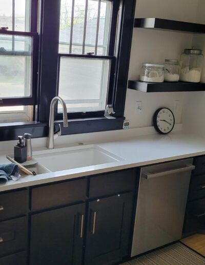 Kitchen with white countertop, dark cabinets, stainless steel dishwasher, and a window.