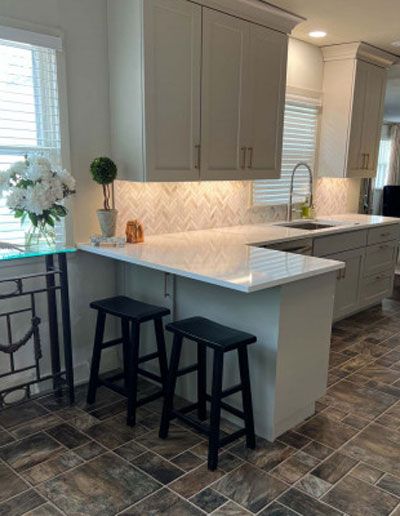Modern kitchen with light gray cabinets, white countertops, and two black stools at a counter.
