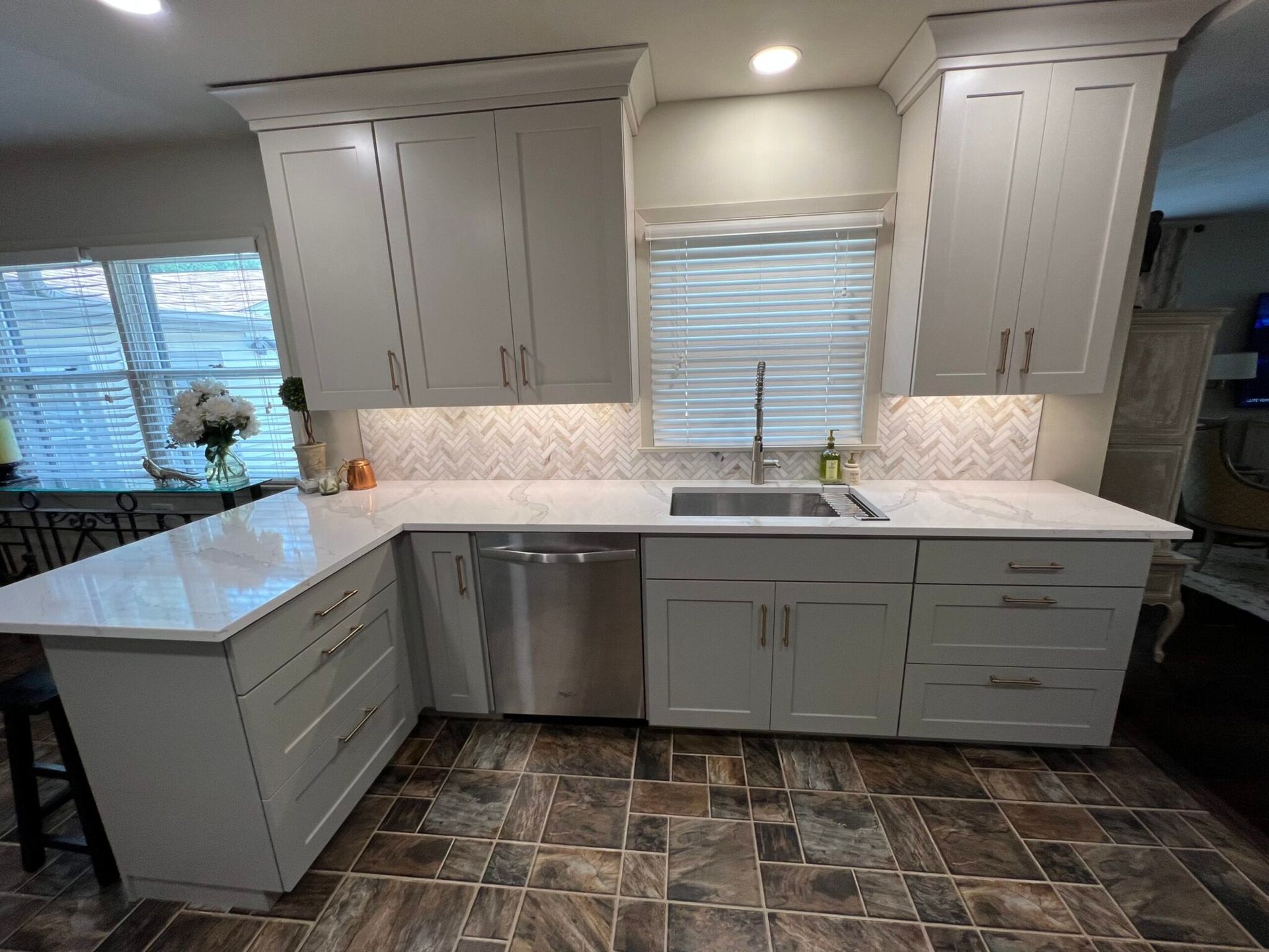 L-shaped kitchen with white cabinets, light countertops, stainless steel appliances, and brown tile flooring.