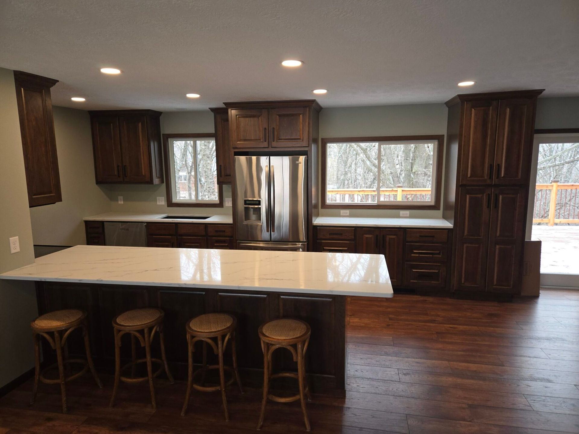 Kitchen with dark wood cabinets, white countertop island, stainless steel refrigerator, and wood floor.