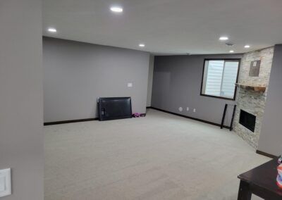 Empty finished basement with neutral walls, carpet, fireplace, and window.