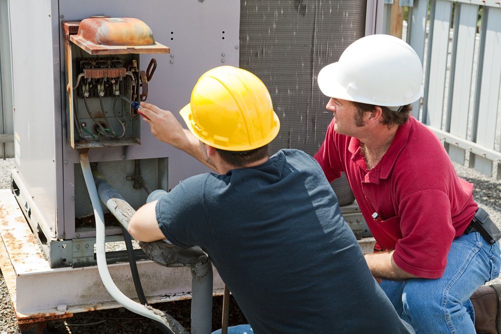 Two men wearing hard hats are working on a machine.