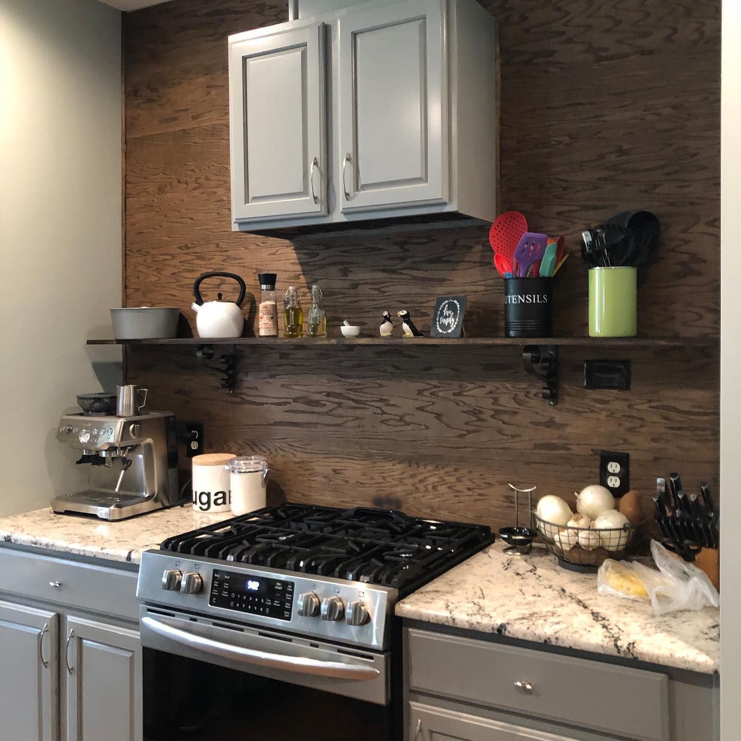 Kitchen with a gray oven, cabinets, and countertops. Brown wood backsplash with floating shelf. Kitchen with a gray oven, cabinets, and countertops. Brown wood backsplash with floating shelf.