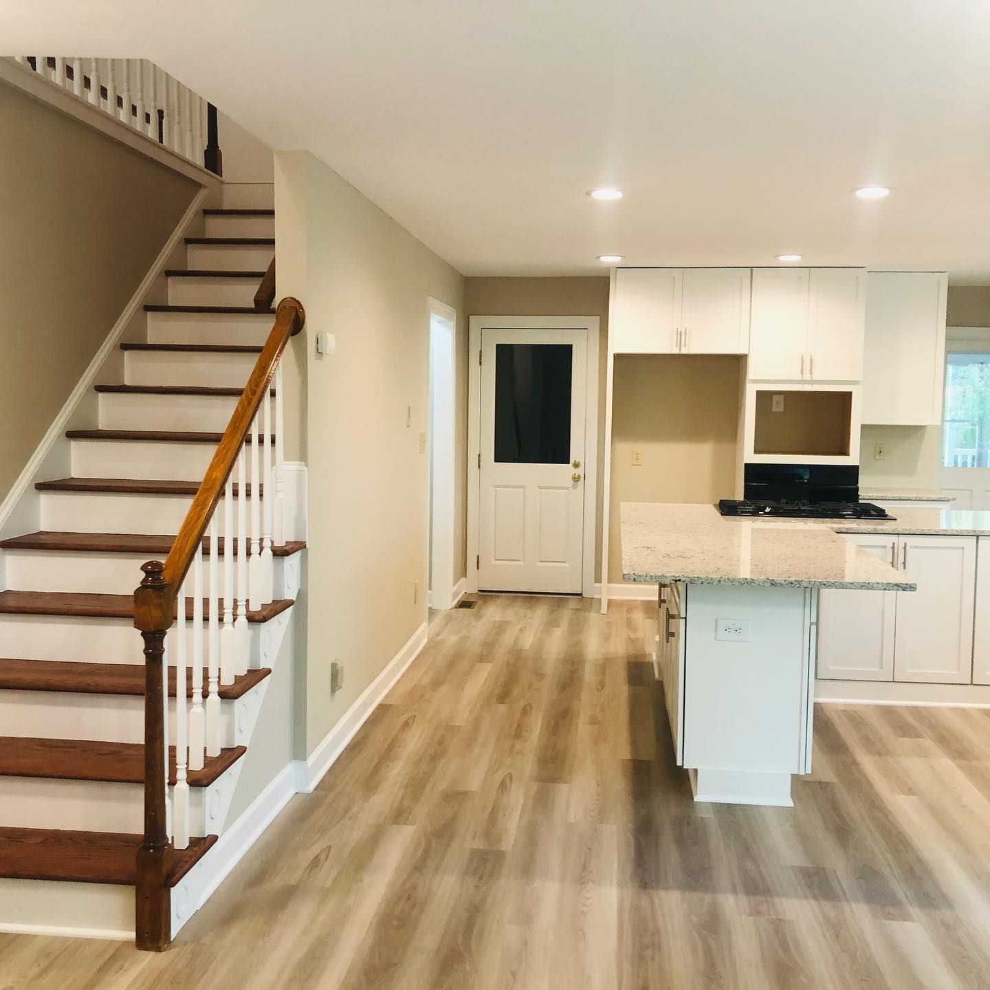 White kitchen with cabinets, island, and overhead lighting. A nearby doorway leads to a bathroom. White kitchen with cabinets, island, and overhead lighting. A nearby doorway leads to a bathroom.