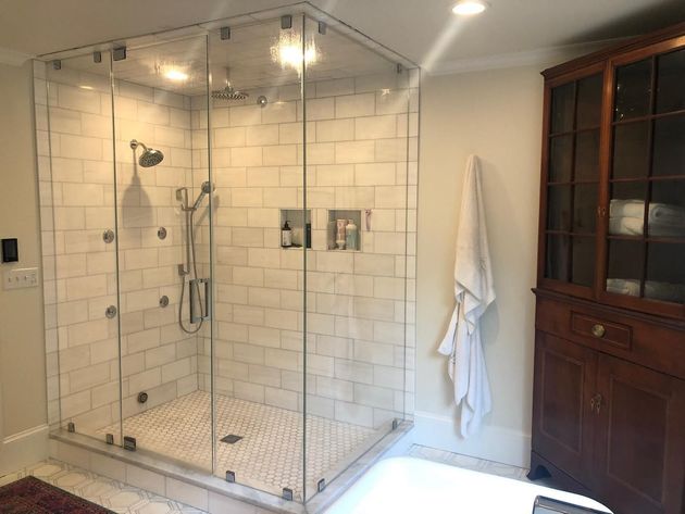 Glass shower enclosure with white tile, toiletries, and a hanging robe.