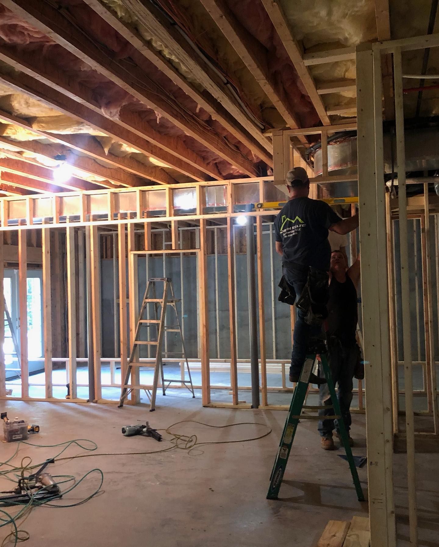 Two construction workers building interior wooden framing inside a room.