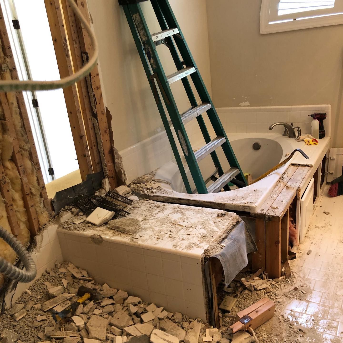 Bathroom renovation: Tub partially demolished, ladder inside, debris on floor. Bathroom renovation: Tub partially demolished, ladder inside, debris on floor.