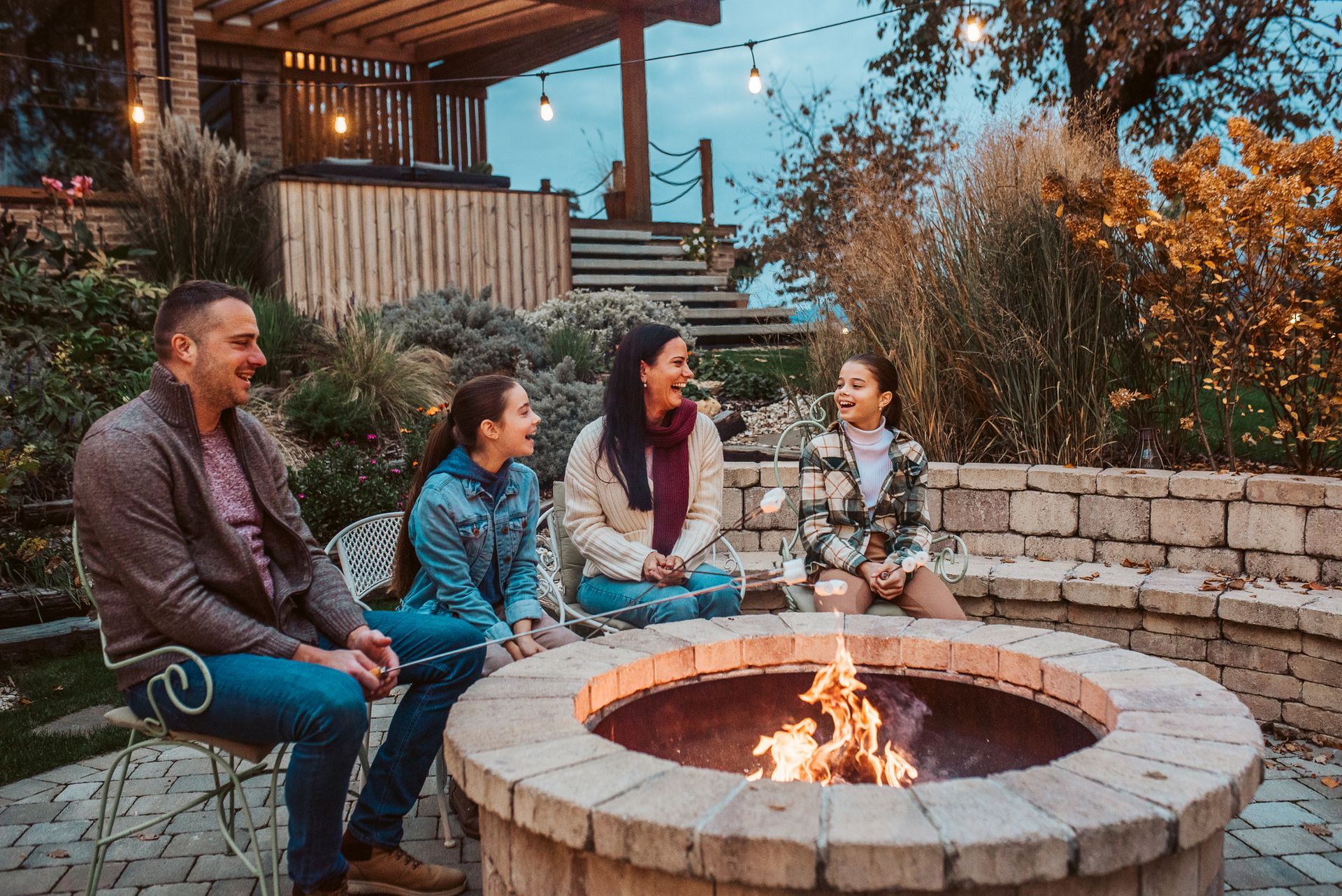 Family gathered around a fire pit, smiling and talking outdoors at dusk. Family gathered around a fire pit, smiling and talking outdoors at dusk.