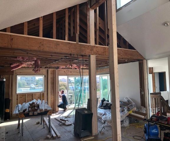 Interior of a house under construction. Exposed beams, drywall, and workers near windows and sliding glass door.