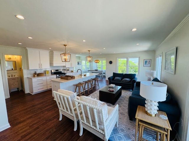 Open-concept living space with white kitchen, dark sofas, and wood flooring.