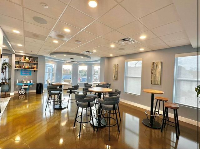 A well-lit cafe interior with round tables, stools, and large windows; neutral colors and wood floors. A well-lit cafe interior with round tables, stools, and large windows; neutral colors and wood floors.