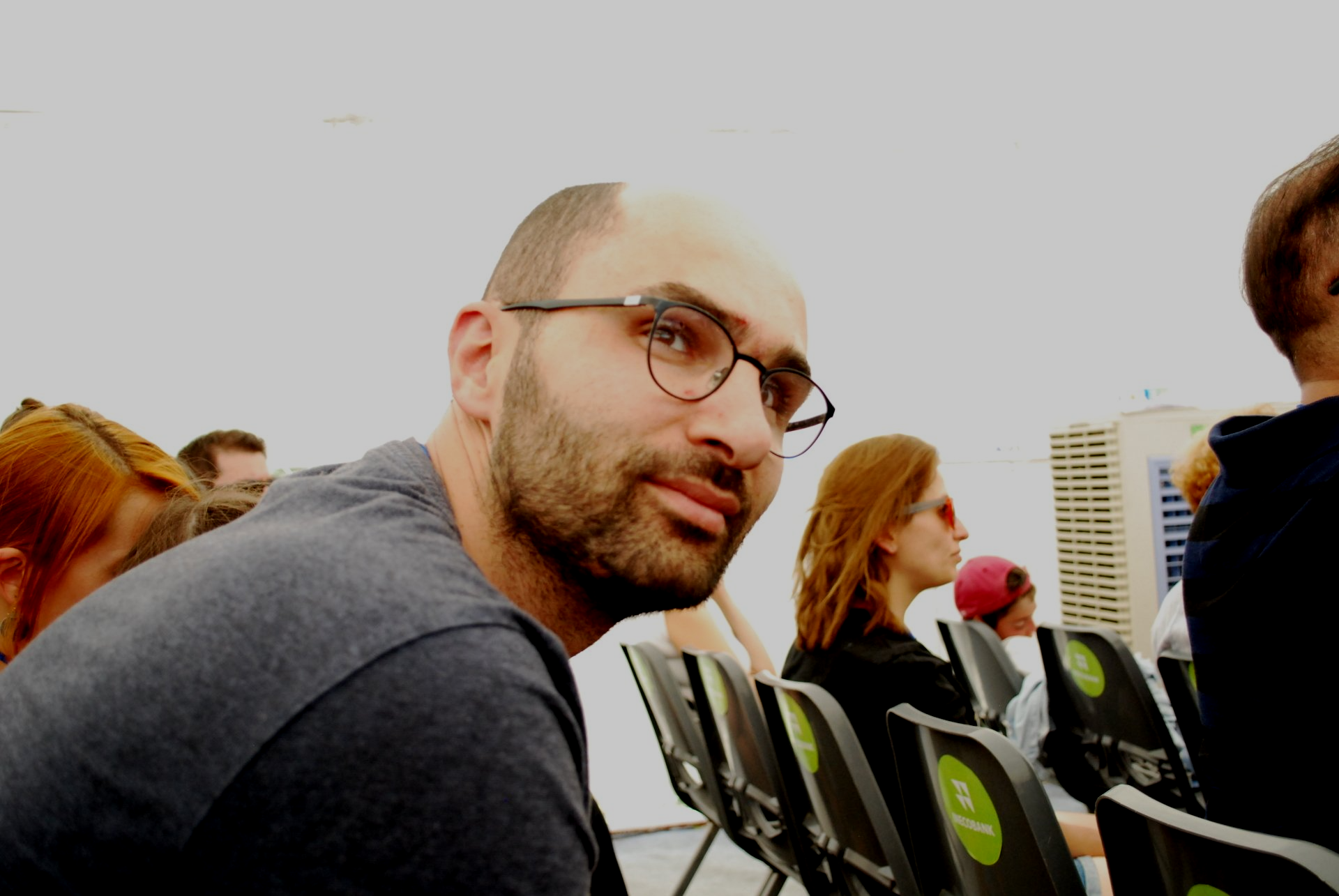 A man wearing glasses sits in a row of chairs