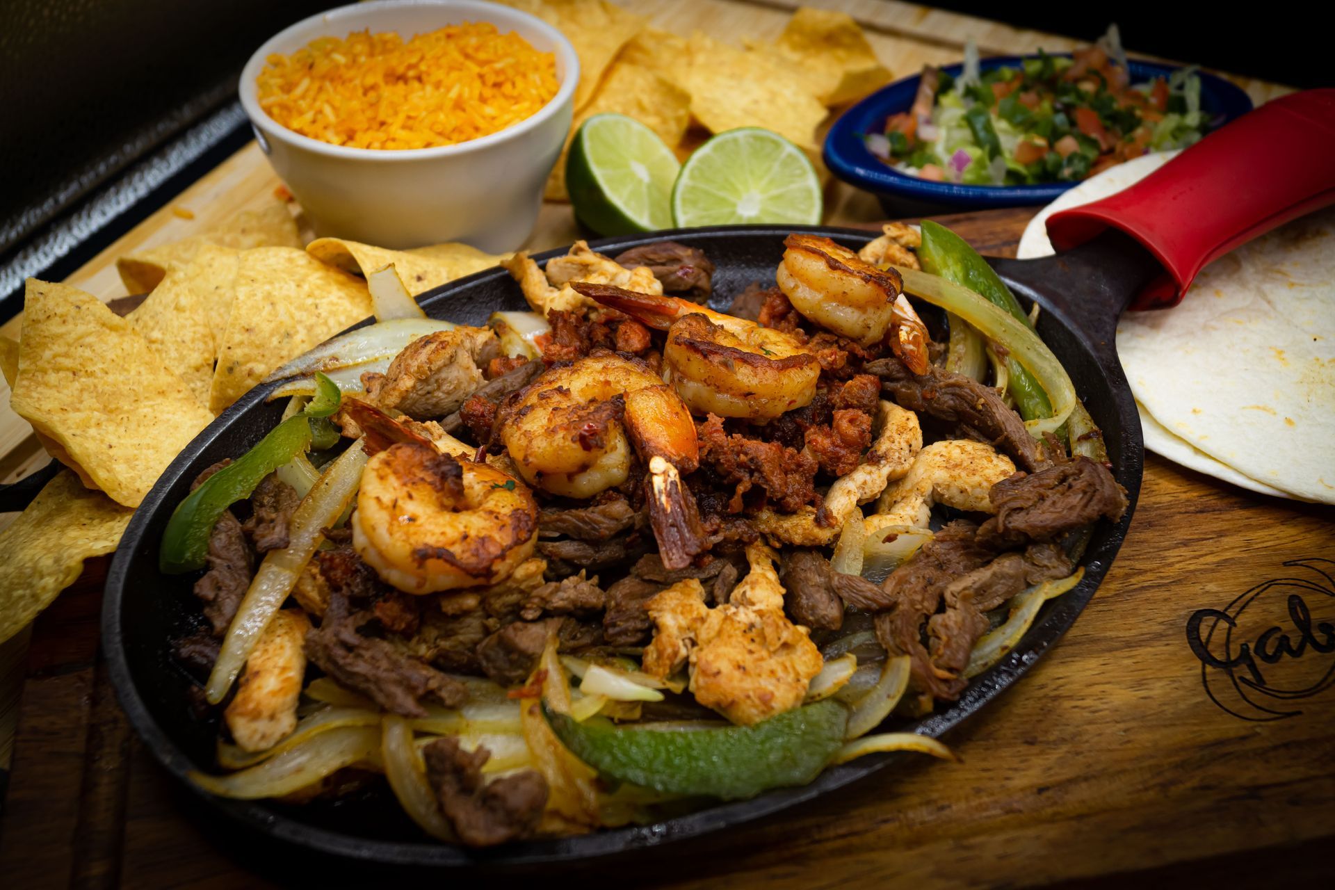 A red plate topped with meat , shrimp , rice and guacamole.