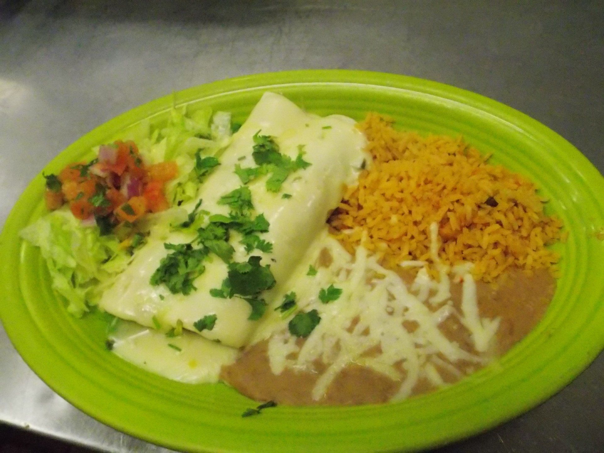 A green plate topped with a burrito , rice and beans.