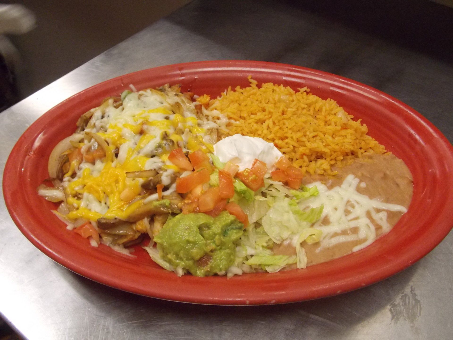 A plate of mexican food with rice and guacamole on a table.