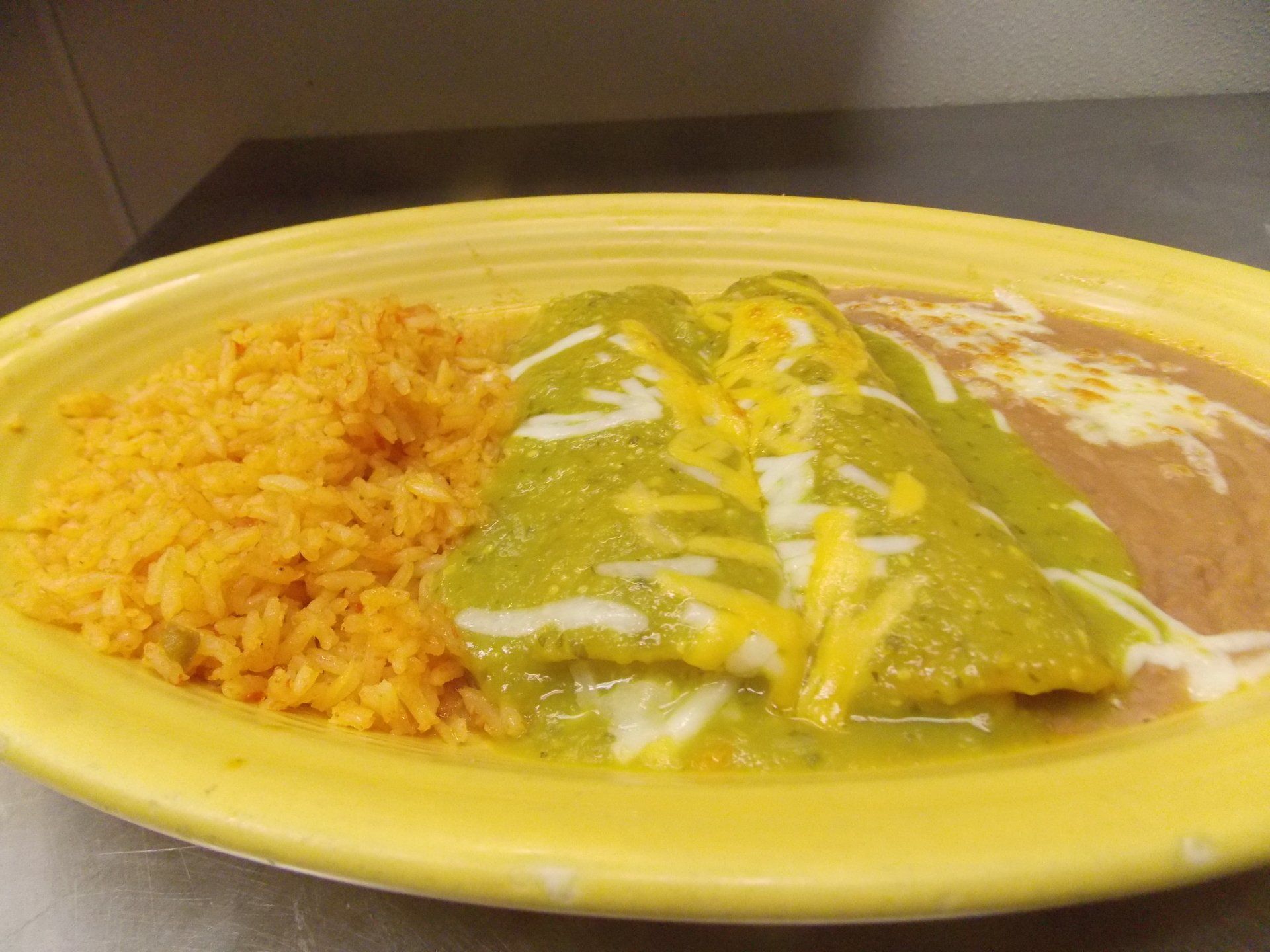 A yellow plate topped with rice and enchiladas on a table.