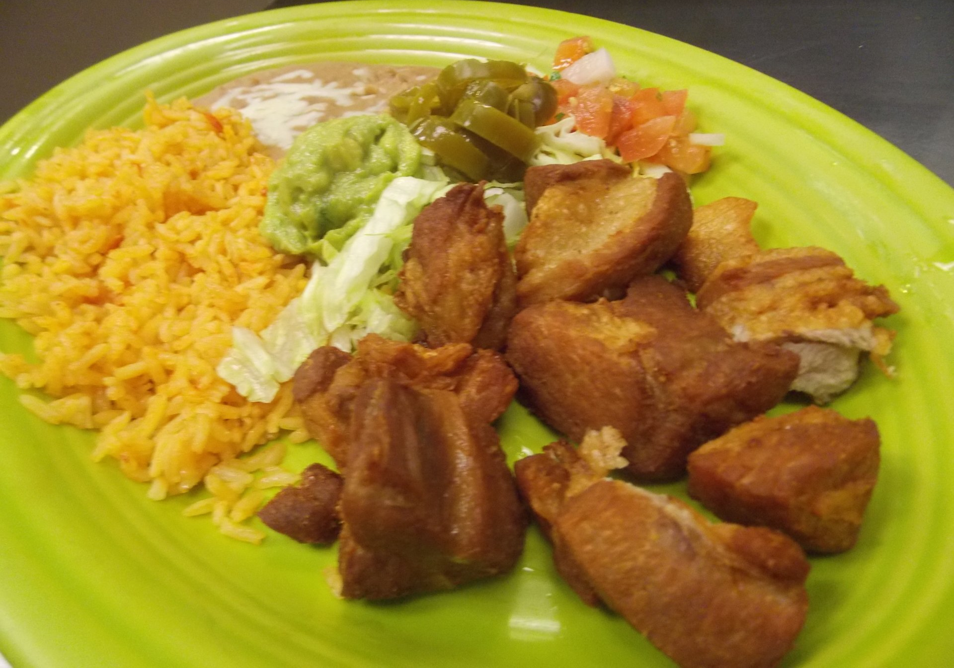 A green plate topped with fried meat , rice and guacamole.