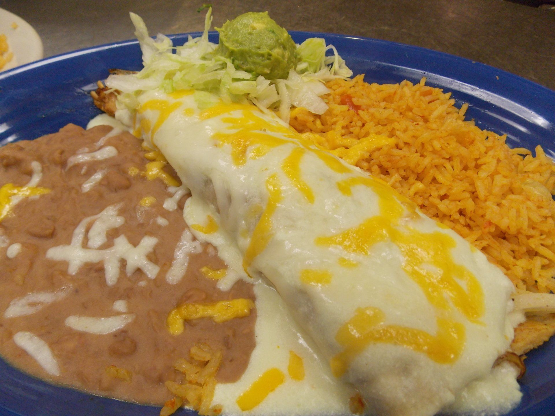 A blue plate topped with a burrito , beans , rice and guacamole.