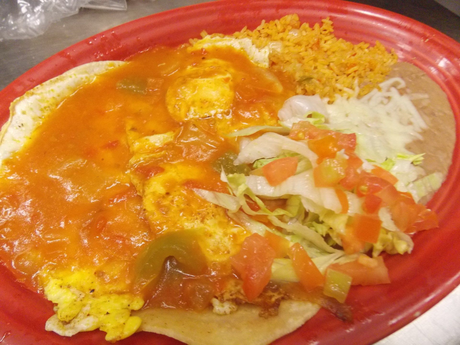 A red plate topped with a tortilla , eggs , rice and vegetables.