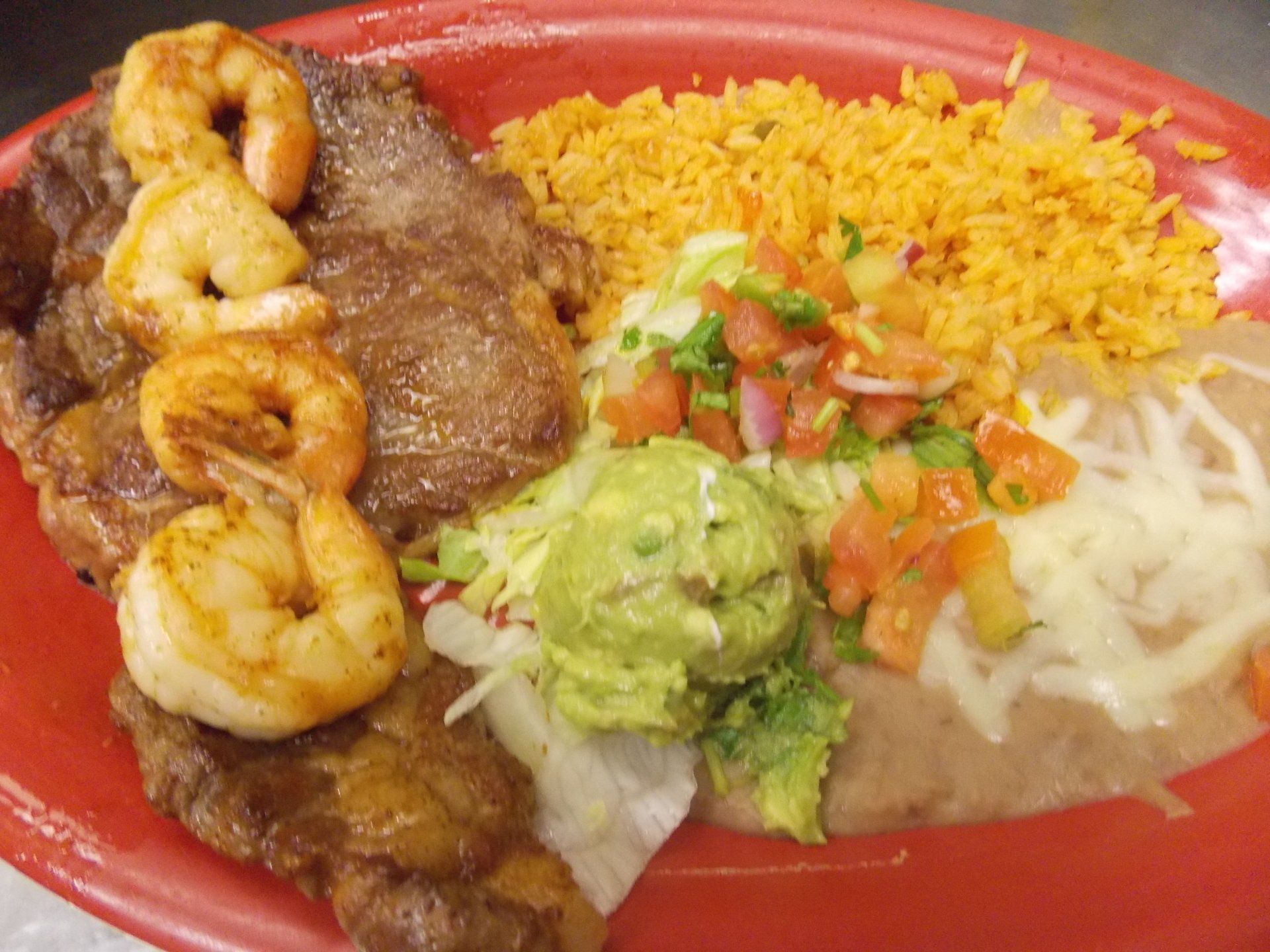 A red plate topped with steak , shrimp , rice and guacamole.