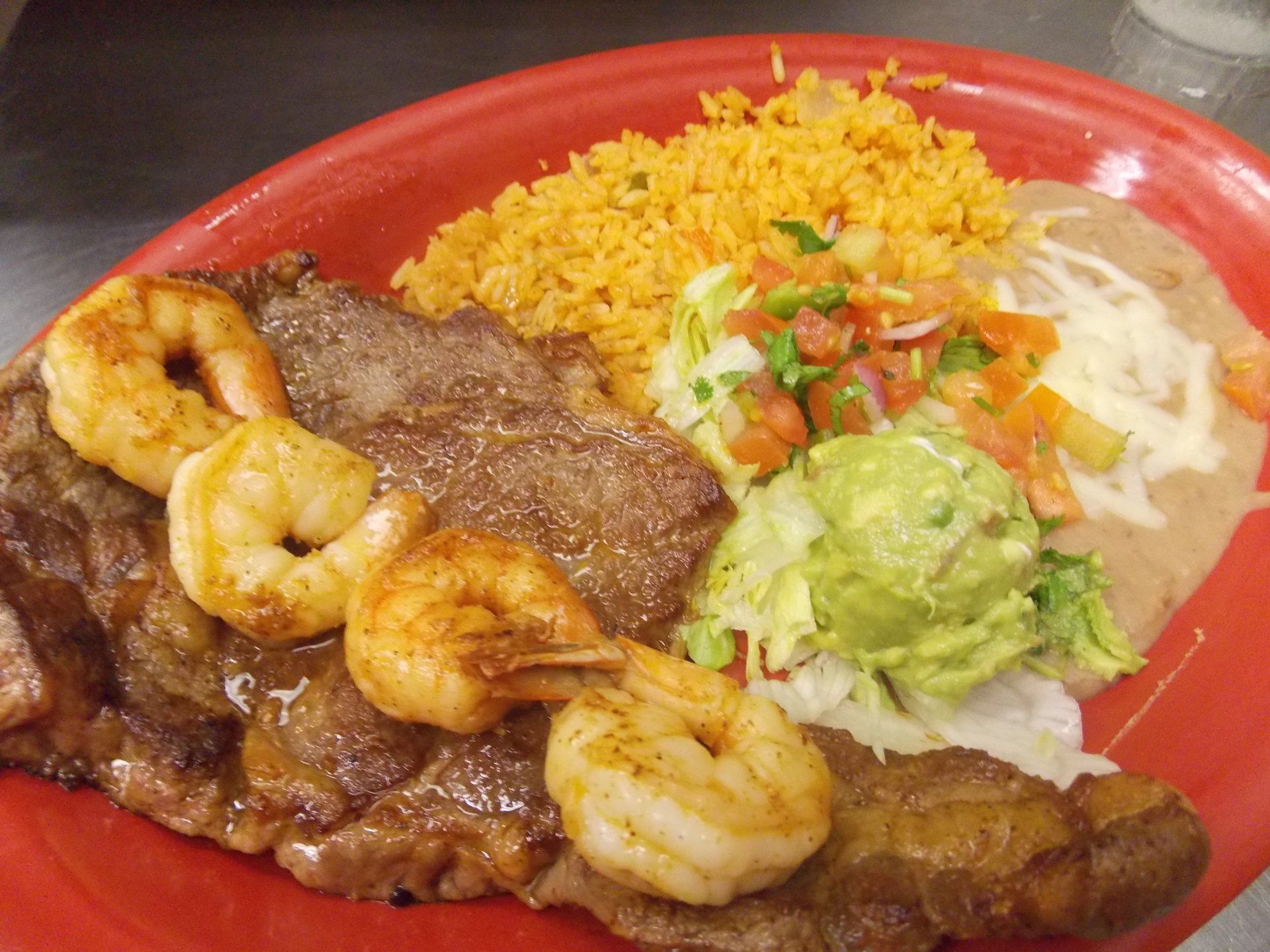 A red plate topped with meat , shrimp , rice and guacamole.