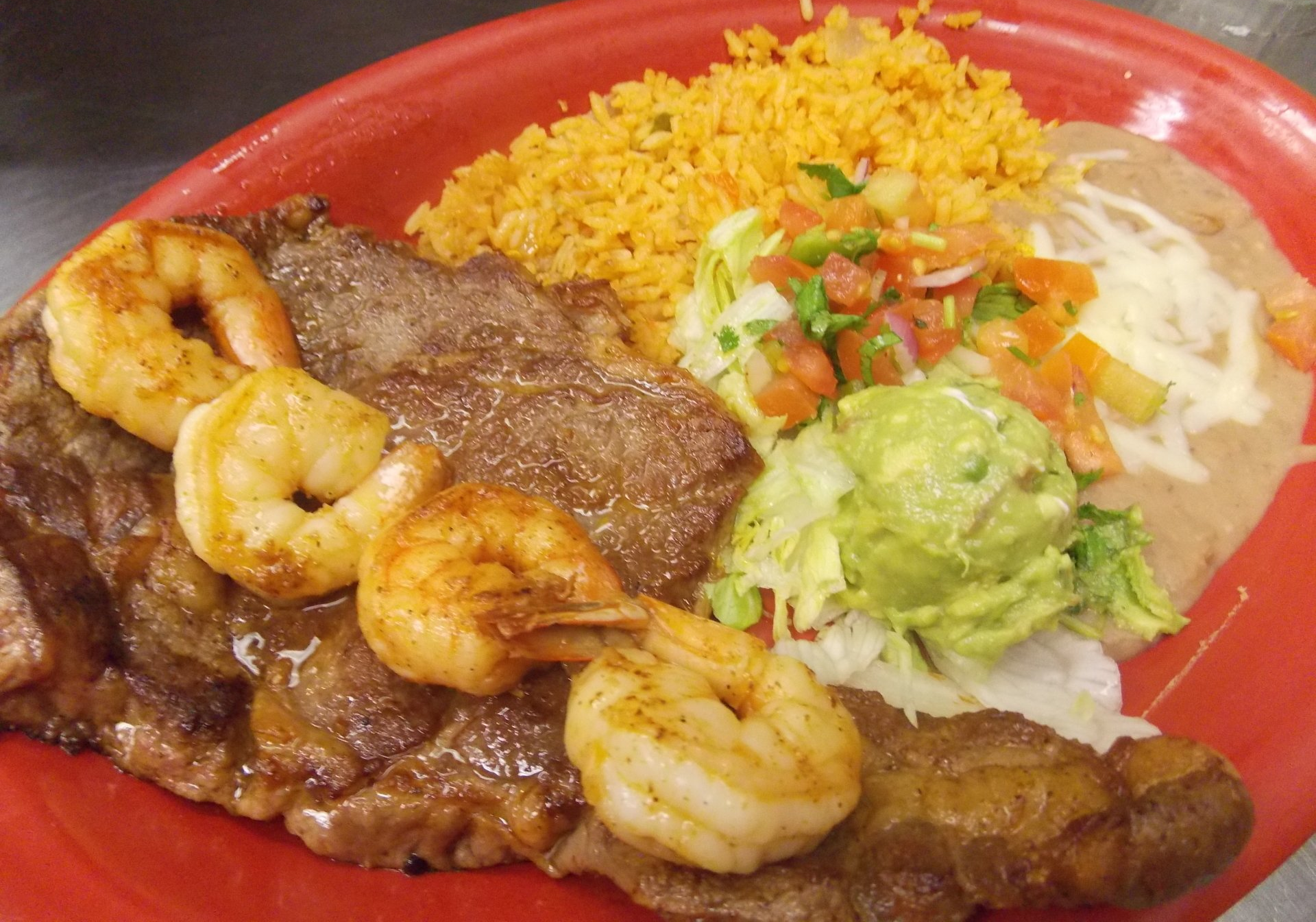 A red plate topped with meat , shrimp , rice and guacamole.