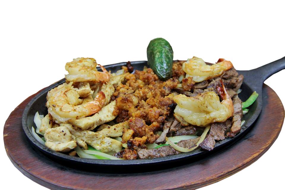 A skillet filled with meat and shrimp on a wooden cutting board.