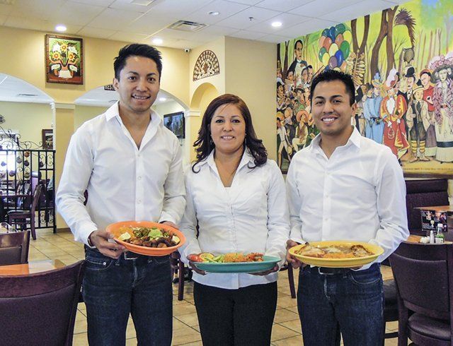 Three people holding plates of food in a restaurant
