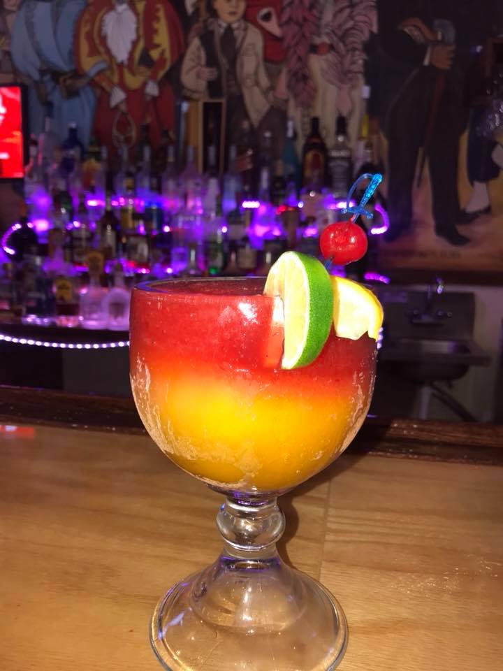 A margarita with a cherry on top of it is on a bar.