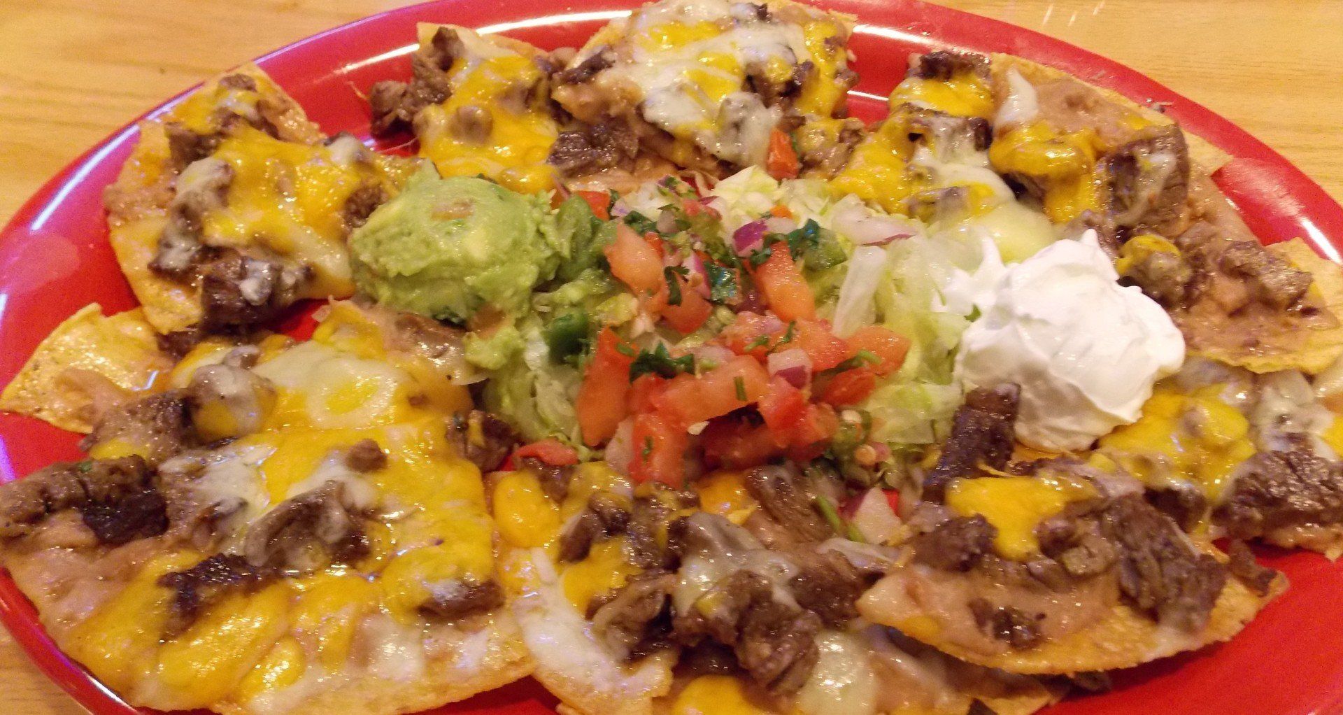 A red plate topped with nachos , guacamole , sour cream and salsa.