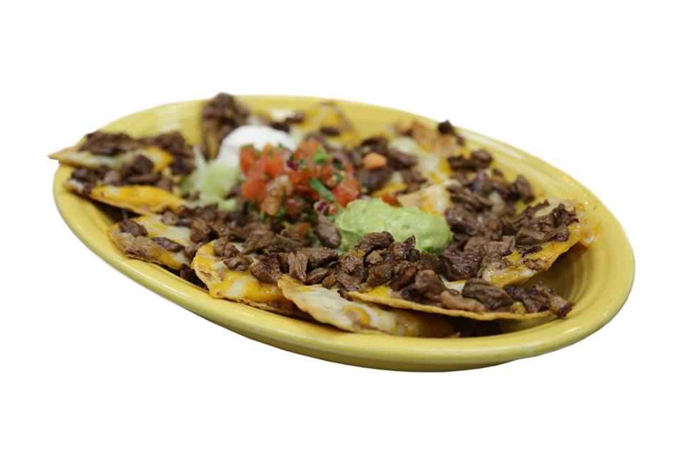A plate of nachos with guacamole and sour cream on a white background.