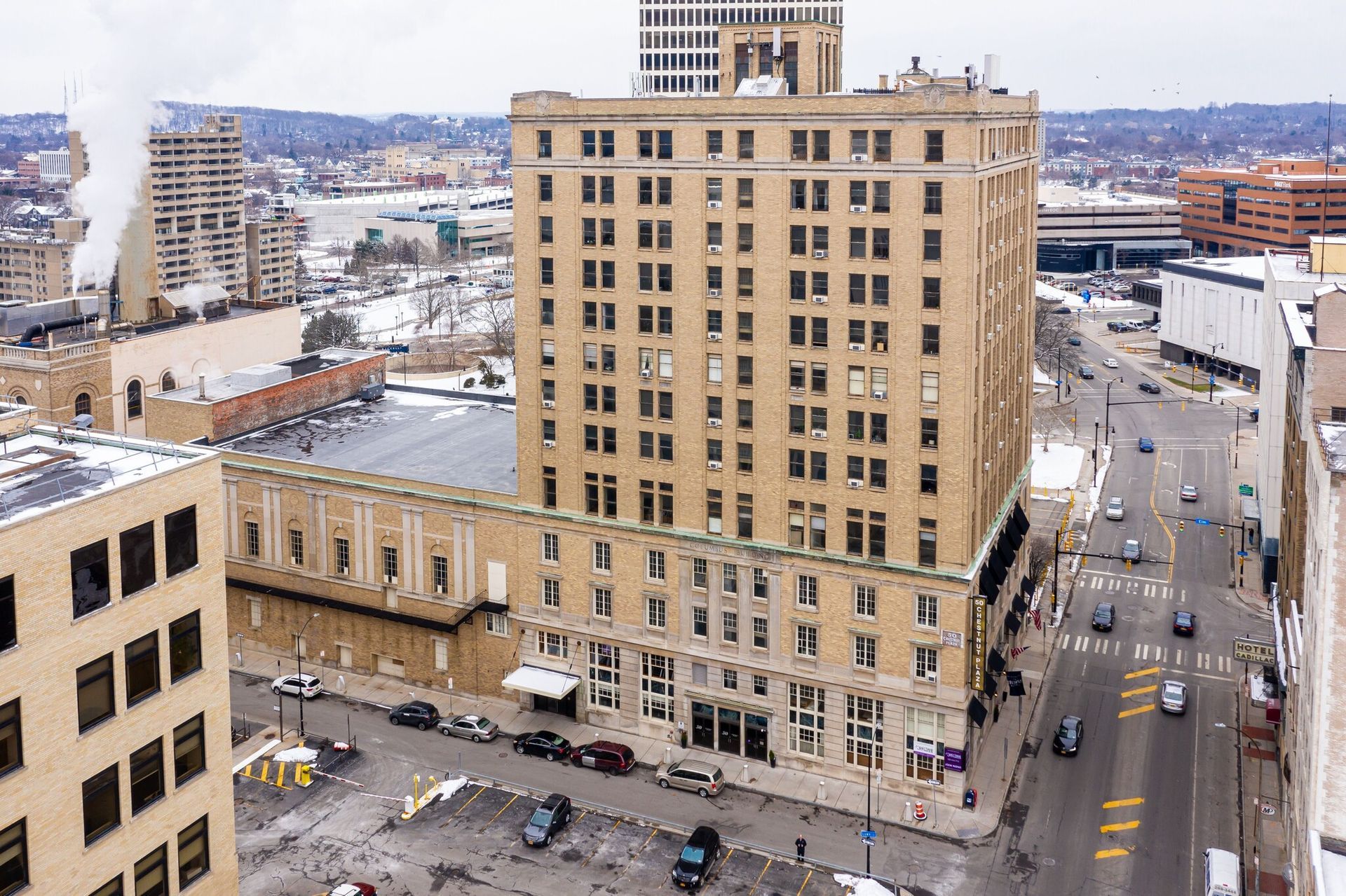 Aerial shot of the Columbus Building, with snow on ground. Cars on street, other buildings in background.