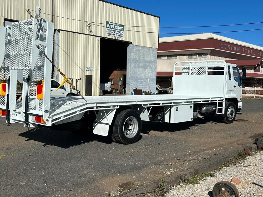 A White Flatbed Truck Is Parked in Front of A Building — EJF Welding in Dubbo, NSW