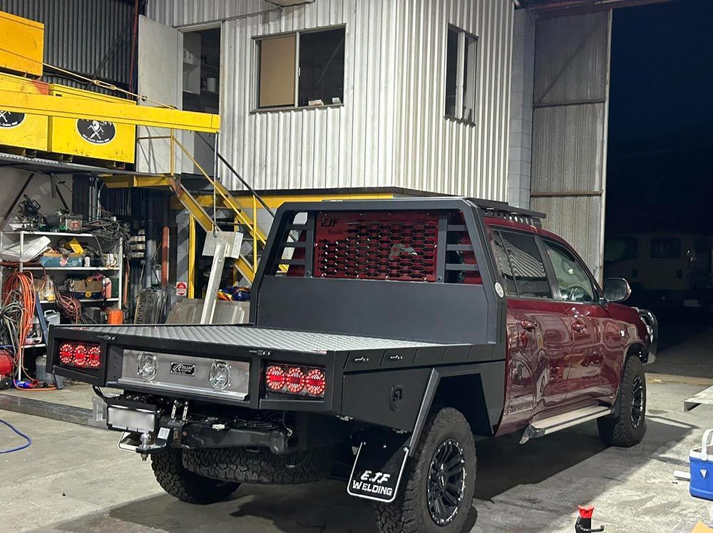 A red truck with a flat bed is parked in front of a building.