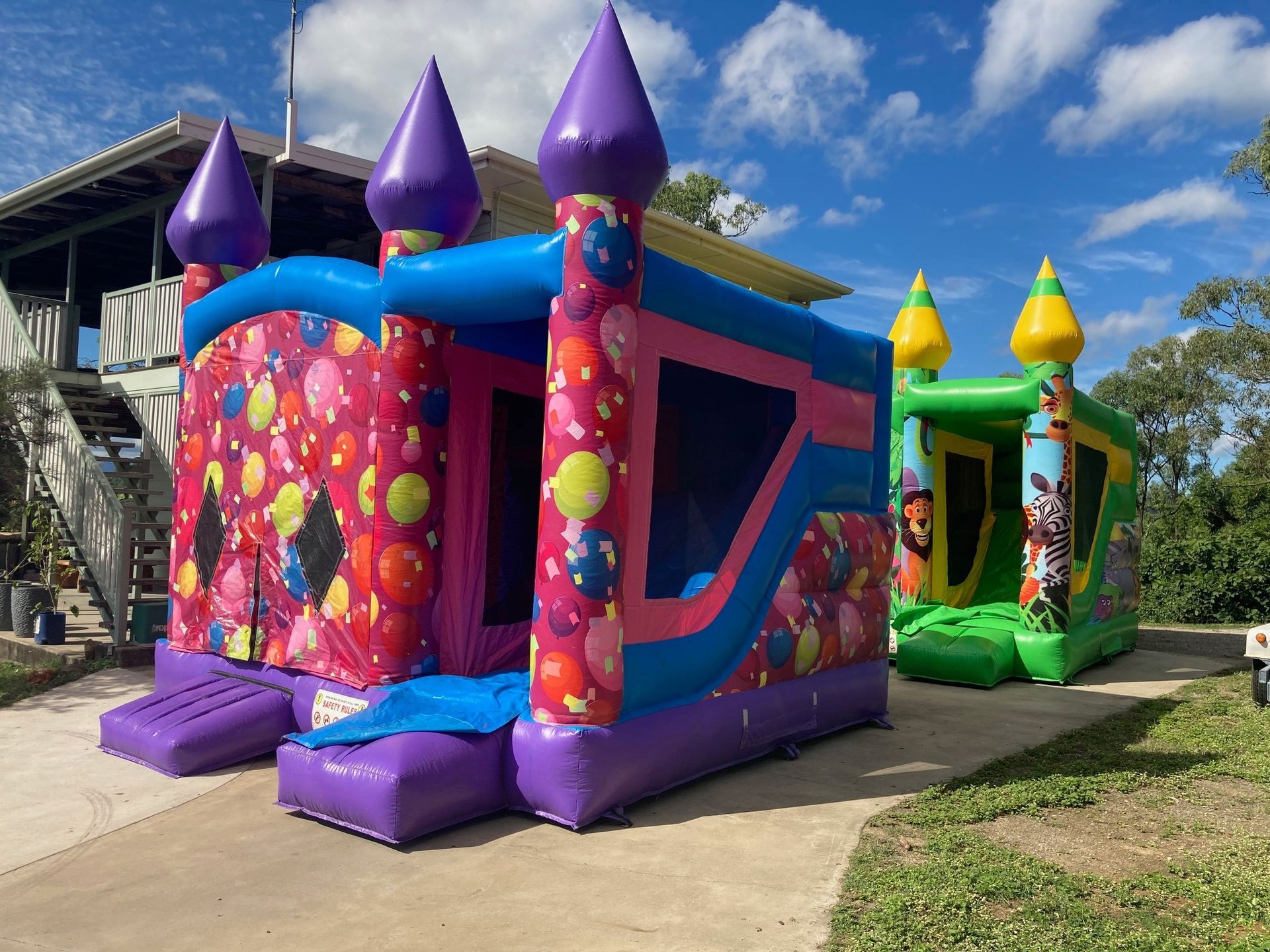 Two Bouncy Houses Are Parked In Front Of A House — Rides N Slides In Townsville, QLD