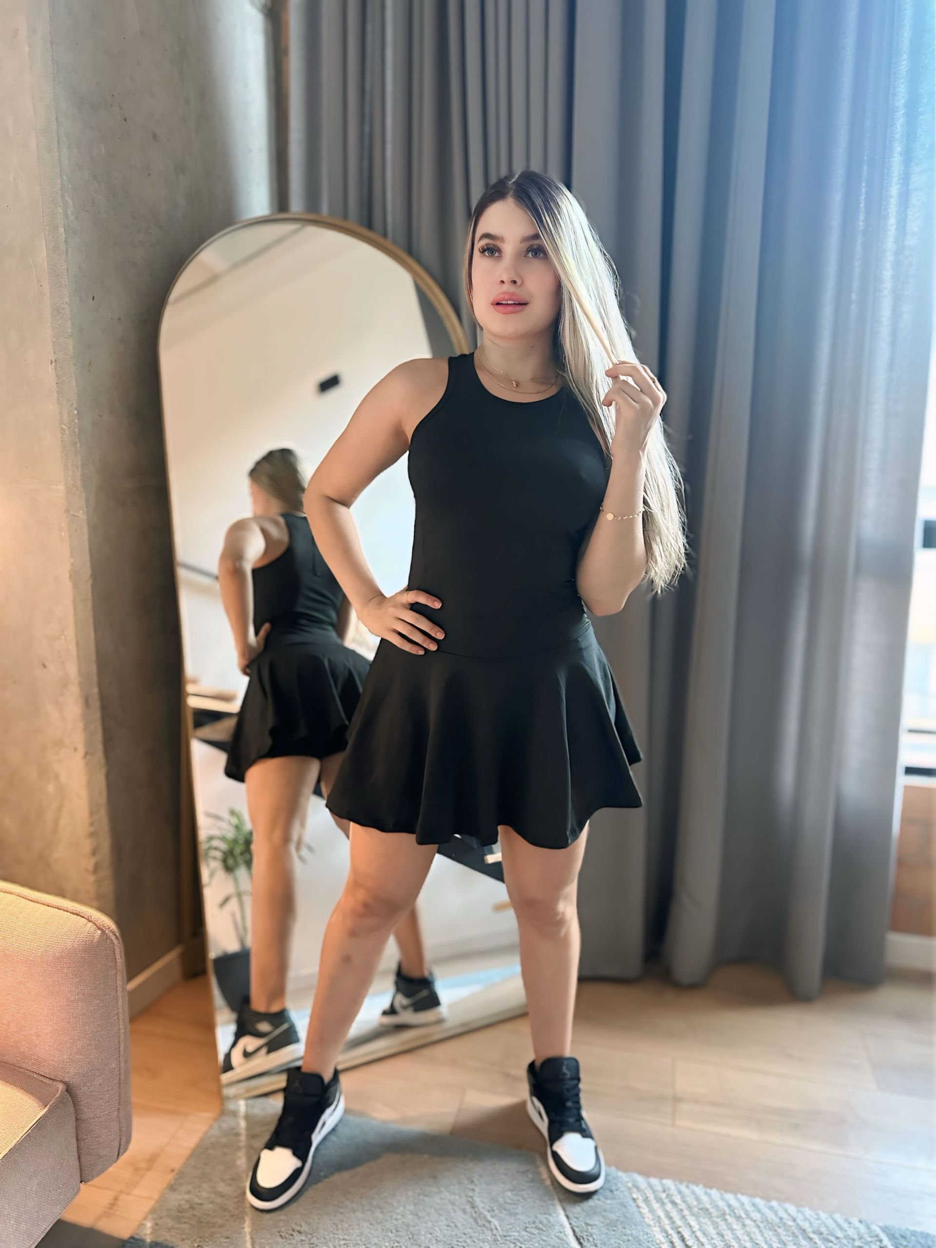 A woman in a black dress is standing in front of a mirror.