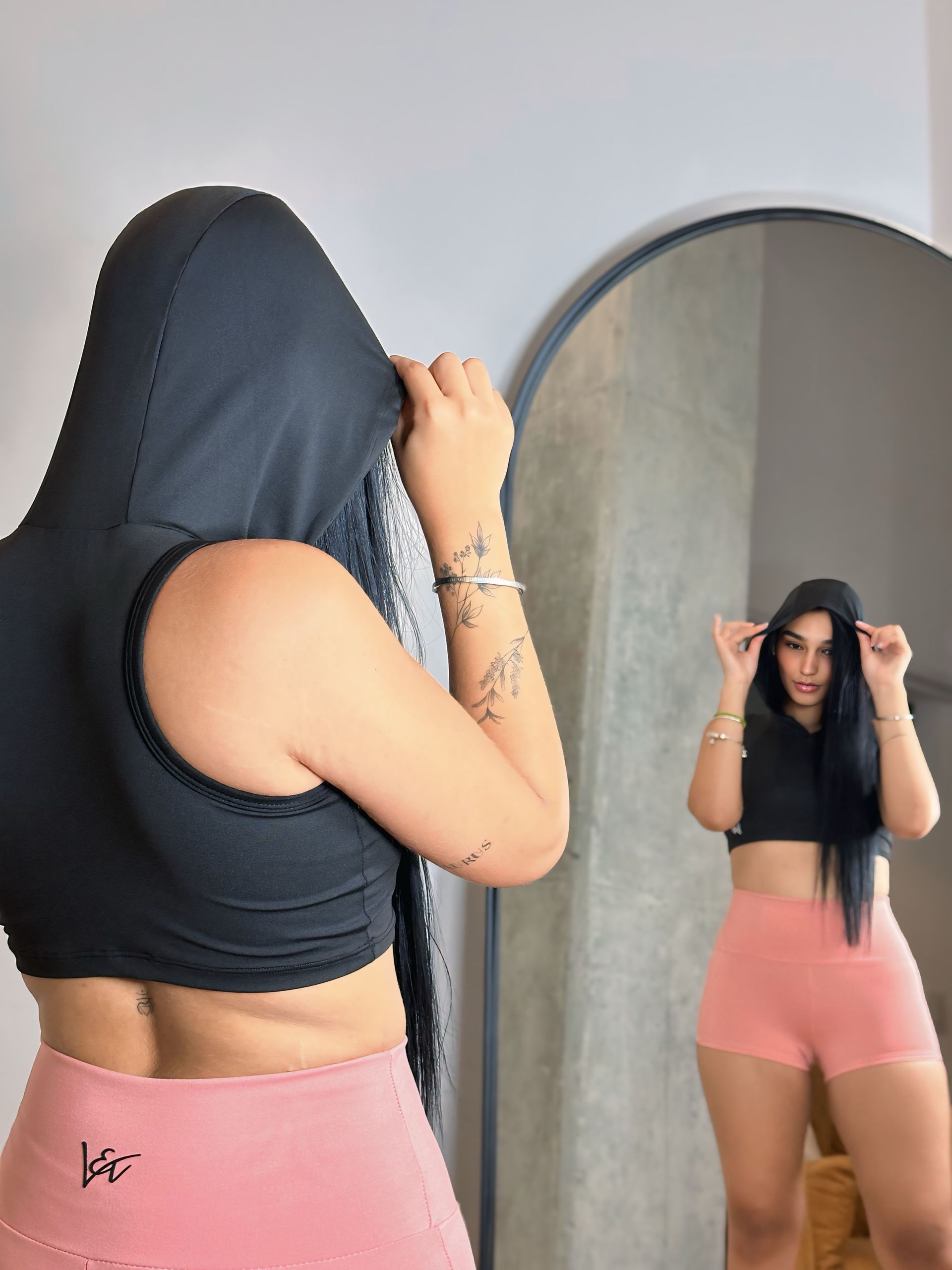 A woman wearing a black crop top and pink shorts is standing in front of a mirror.