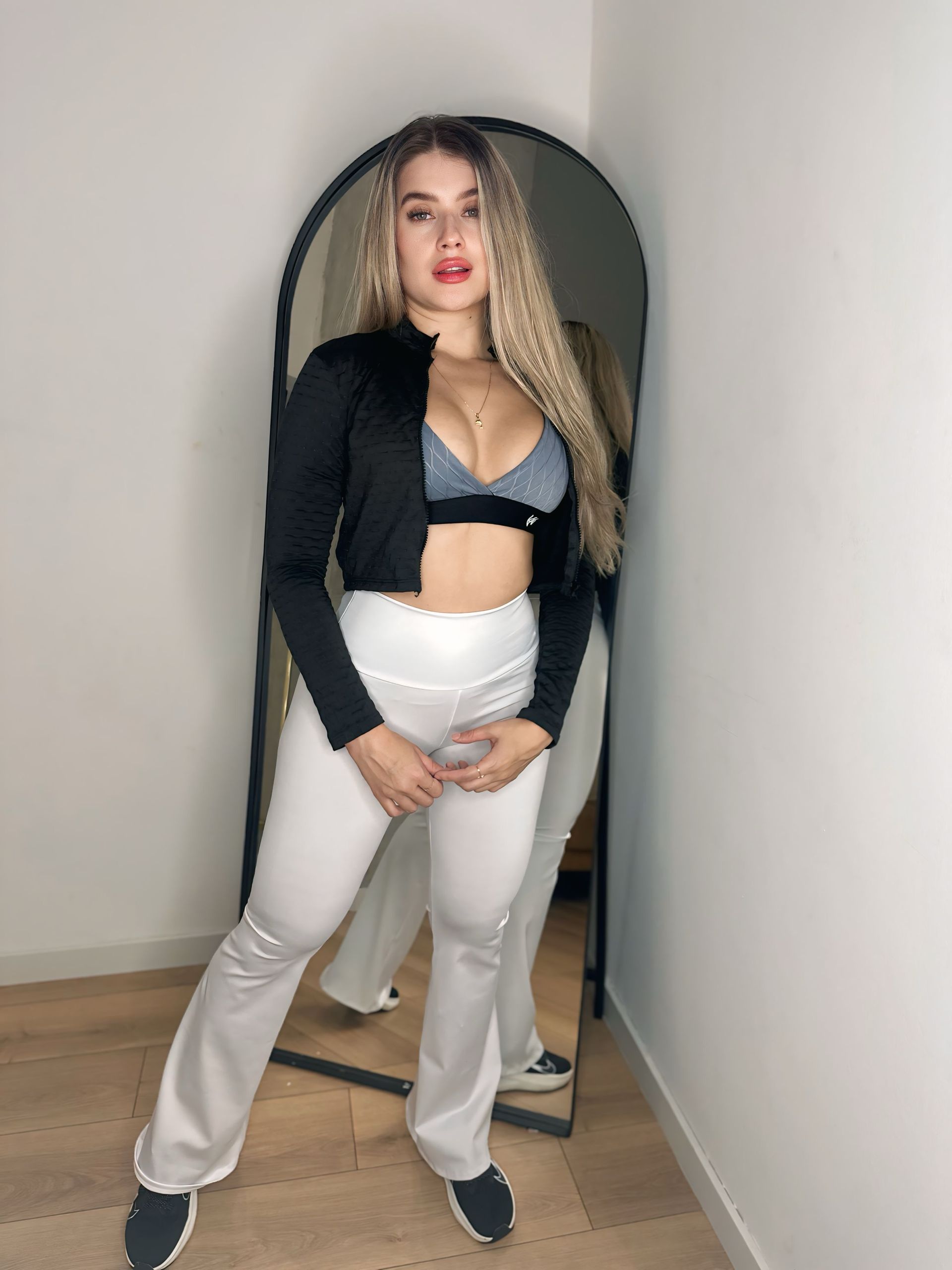 A woman in a black crop top and white pants is standing in front of a mirror.